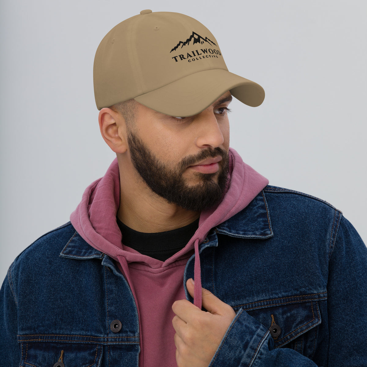 Man wearing a khaki Trailwood Mountain dad hat with the black embroidered mountain-range logo, right-front view